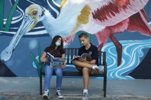 students sitting on bench in front of wall mural